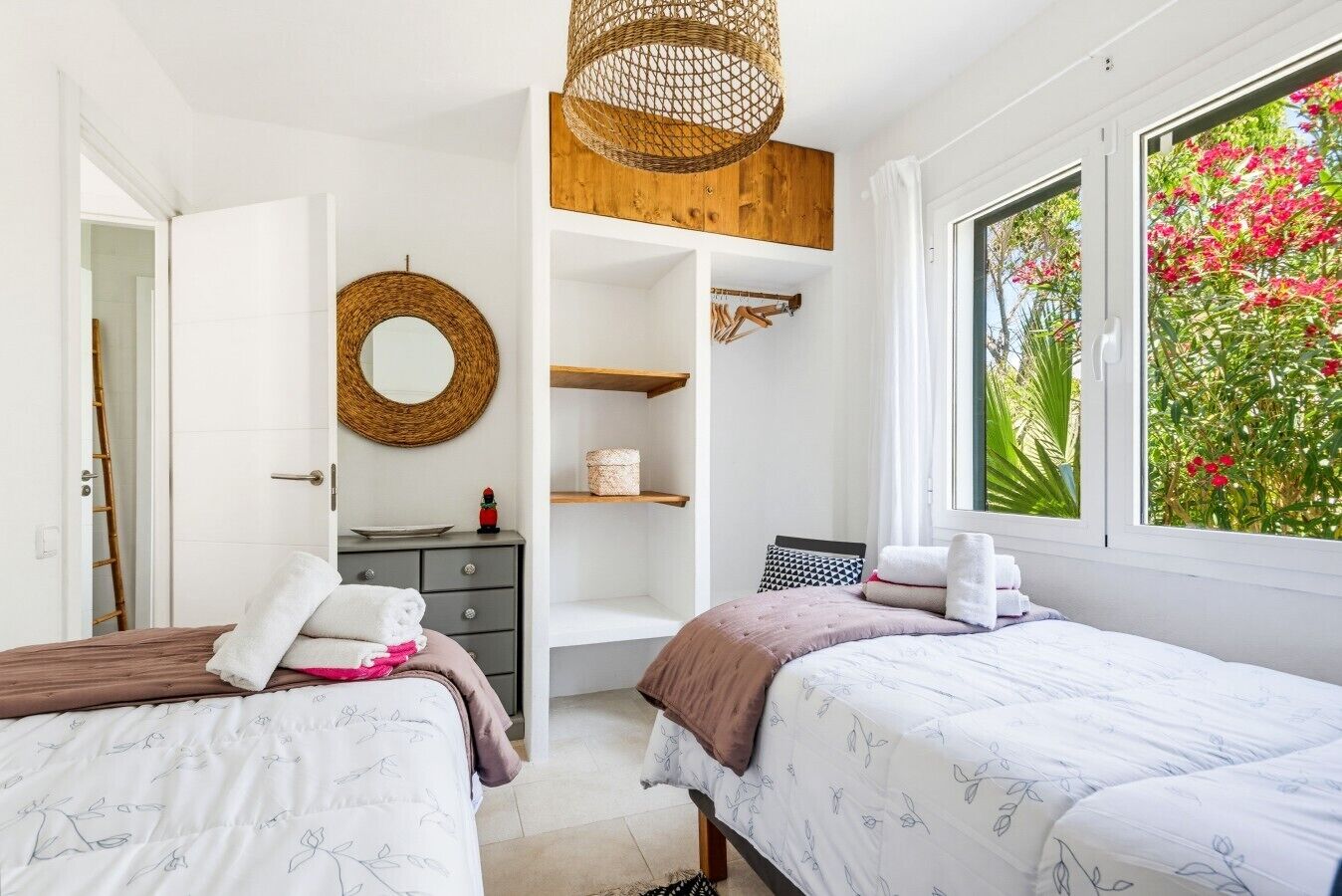 Un dormitorio con dos camas, un aparador, un espejo y una ventana con vistas a zonas verdes.
