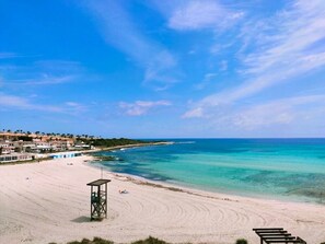 Une plage avec une eau turquoise et limpide, une tour de surveillance des sauveteurs et des bâtiments en arrière-plan.