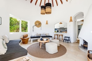 A modern living room with a sofa, coffee table, and ottoman, a kitchen area with bar stools, and a fireplace.