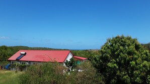 A house with a red roof, surrounded by lush greenery and hills in the background.