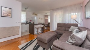 A modern living room with a sofa, ottoman, and a dining area with a kitchen in the background. - 1 bedroom awesome apartment in Biograd na Moru (Biograd na Moru)