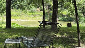 Ein Tisch und ein Stuhl aus Metall, aufgestellt in einer natürlichen Umgebung mit Fluss und Bäumen im Hintergrund.