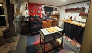 A compact kitchen with a stove, oven, and various appliances. There is a small dining table with a cutting board. The kitchen has wooden cabinets and a tiled backsplash. - Charming waterfront getaway Along Harmon Creek (Huntsville)
