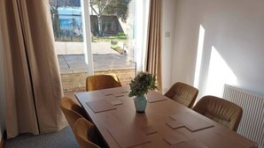 A conference room with a wooden table, four chairs, a vase with flowers, and a view of the outside through large windows. - Charming 3-bed House in Birmingham Near nec & hs2 (Birmingham)
