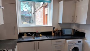 A compact kitchen with a sink, stove, and a built-in washing machine. - Charming 3-bed House in Birmingham Near nec & hs2 (Birmingham)