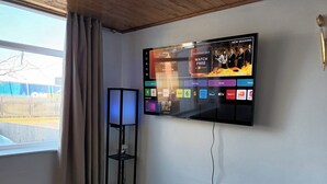 A room with a mounted TV displaying various streaming services, a floor lamp, and a window with curtains. - Charming 3-bed House in Birmingham Near nec & hs2 (Birmingham)