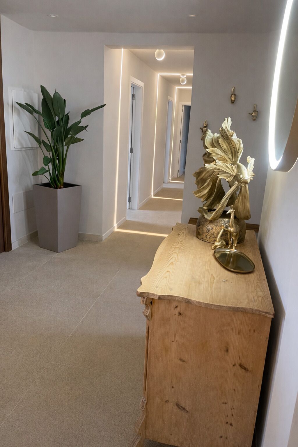 Un couloir agrémenté d’une plante en pot, d’une console en bois ornée d’objets décoratifs et d’un luminaire moderne.