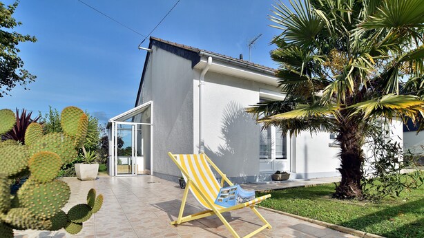 A modern house with a patio, a yellow striped beach chair, and various plants including cacti. - Karome (Saint-Coulomb)