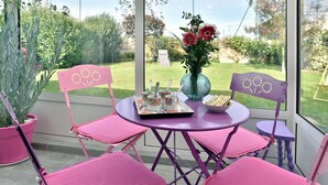 A patio with pink chairs and a table, a vase with flowers, and a view of a garden. - Karome (Saint-Coulomb)