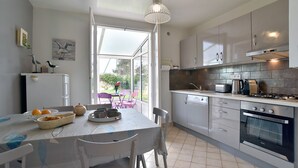 A modern kitchen with white cabinetry, a dining table with chairs, a large window, and a hanging light fixture. - Karome (Saint-Coulomb)