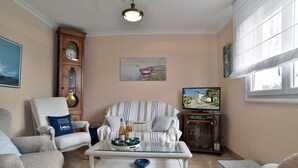 A living room with a sofa, armchairs, a coffee table, a television, a clock, and a painting. - Karome (Saint-Coulomb)