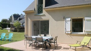 Une maison dotée d’un patio comprenant une table et des chaises, un petit jardin et un garage.