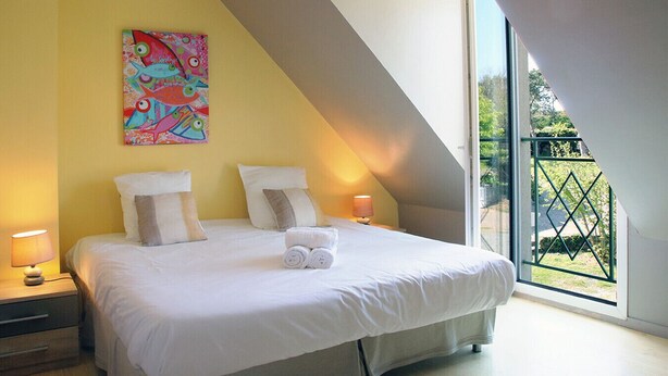 Une chambre à coucher avec un grand lit, deux lampes de chevet, un tableau coloré et une vue sur un jardin par la fenêtre.