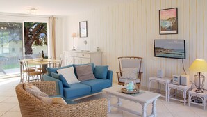 Un salon avec un canapé bleu, des meubles en osier, une table basse blanche et un téléviseur posé sur un meuble.