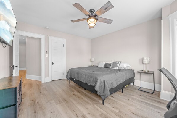 A bedroom with a bed, a ceiling fan, a nightstand, and a desk.
