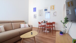 Una sala de estar moderna con un sofá, una mesa de centro y un comedor con sillas y una mesa. Hay obras de arte en la pared y un espejo.