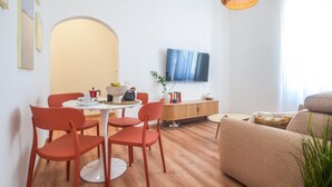 Una sala moderna con una mesa de comedor redonda, sillas rojas, un sofá beige, un televisor de pantalla plana y un mueble de madera.