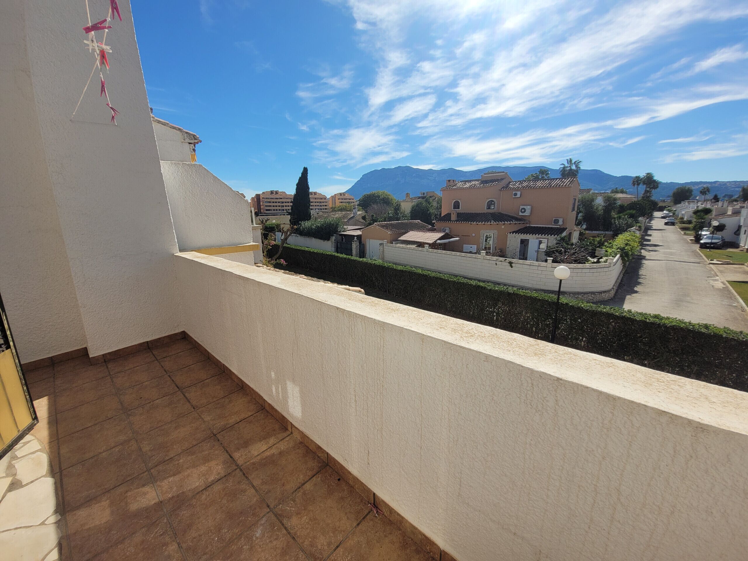 Uma varanda com vista para uma rua residencial, um arbusto e montanhas ao longe.