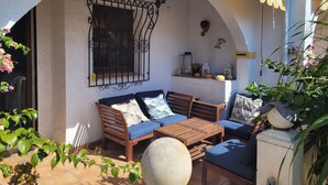 An outdoor seating area with a wooden bench and table, a small shelf with decorative items, and a potted plant. - Anacasa Duplex Marineta Bot DUP2136 (Denia)