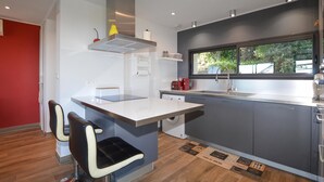 Une cuisine moderne dotée d’un îlot central, d’un lave-vaisselle encastré et d’une fenêtre donnant sur un espace verdoyant.