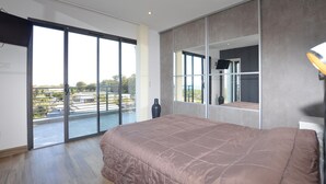 Une chambre dotée d’un grand lit, d’une porte-fenêtre coulissante donnant sur un balcon et d’un grand miroir qui reflète la pièce.