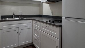 A kitchen with white cabinets, a microwave, a refrigerator, and a black countertop. - Las Palmas Airport Inn (Tucson)