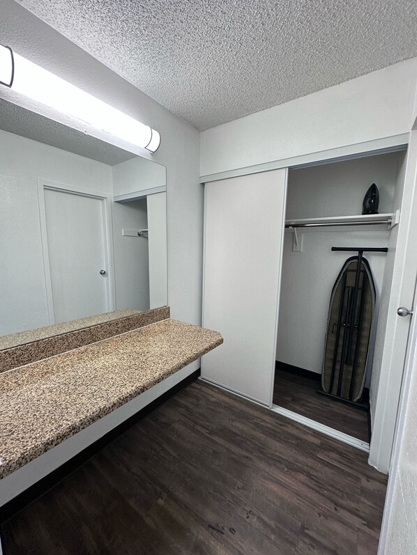 Et badeværelse med bordplade i granit, et spejl, en bruser og et walk-in closet med en knagerække.