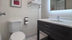 A bathroom with a toilet, a sink with a mirror, and a towel rack. - Las Palmas Airport Inn (Tucson)
