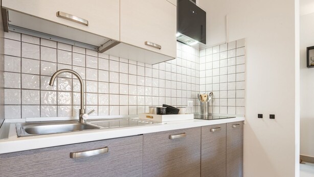 A modern kitchen with a stainless steel sink, white tiled backsplash, and wooden cabinets.