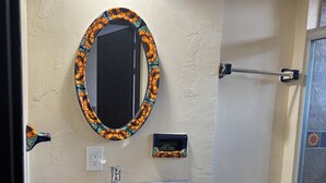 Un baño con un espejo redondo, lavamanos e inodoro.
