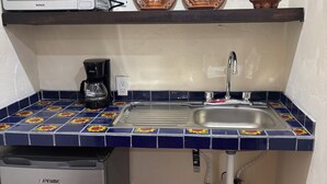 Cocina compacta equipada con microondas, cafetera, lavamanos y refrigerador pequeño.