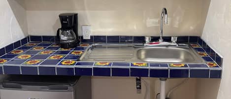 Cocina compacta equipada con microondas, cafetera, lavamanos y refrigerador pequeño.