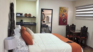 Un dormitorio con cama, mesita de noche, lámpara y vista a la cocina.