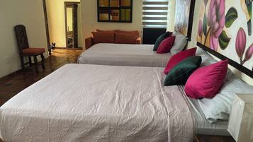 A hotel room with two beds, a wooden floor, a painting on the wall, and a window with blinds.