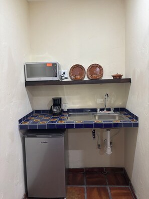 Una cocina compacta con microondas, cafetera, lavamanos y un refrigerador pequeño.