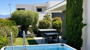A swimming pool with a ladder, surrounded by greenery and a modern building. - Villa "Dolce Vida" golf / lake / spa 6p (Villeneuve-de-la-Raho)