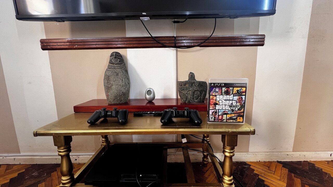 Un'area giochi con una console PS3, dei controller e una custodia di gioco su un tavolo di legno.