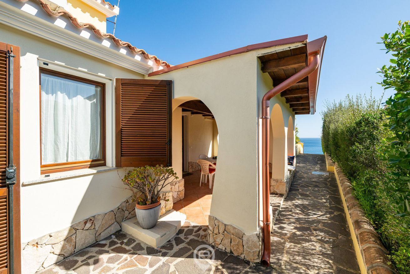 A house with a stone patio, a potted plant, and a view of the sea.
