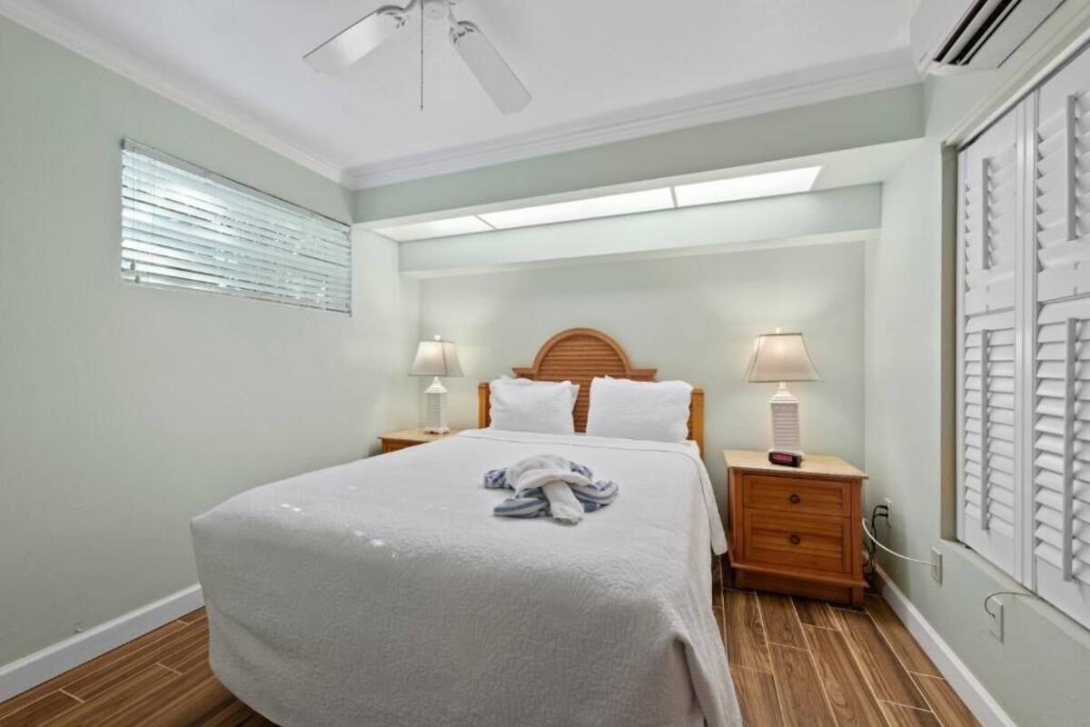A bedroom with a bed, two bedside tables, a ceiling fan, and a window with blinds.