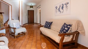 Amplia sala de estar con sofá y sillones, una escalera y una puerta que da a otra habitación.
