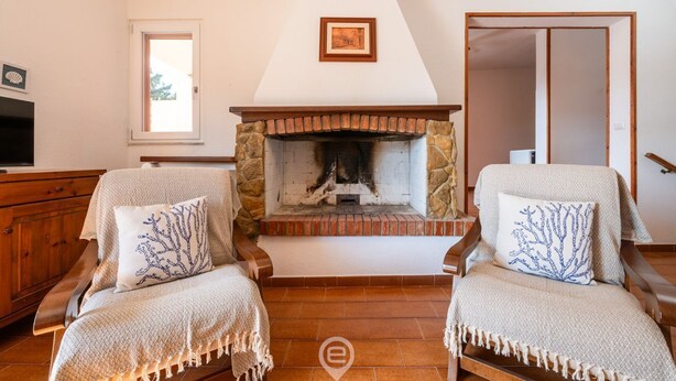 Una sala de estar acogedora con chimenea de piedra, dos sillones con cojines decorativos, un aparador de madera y un ventanal grande.