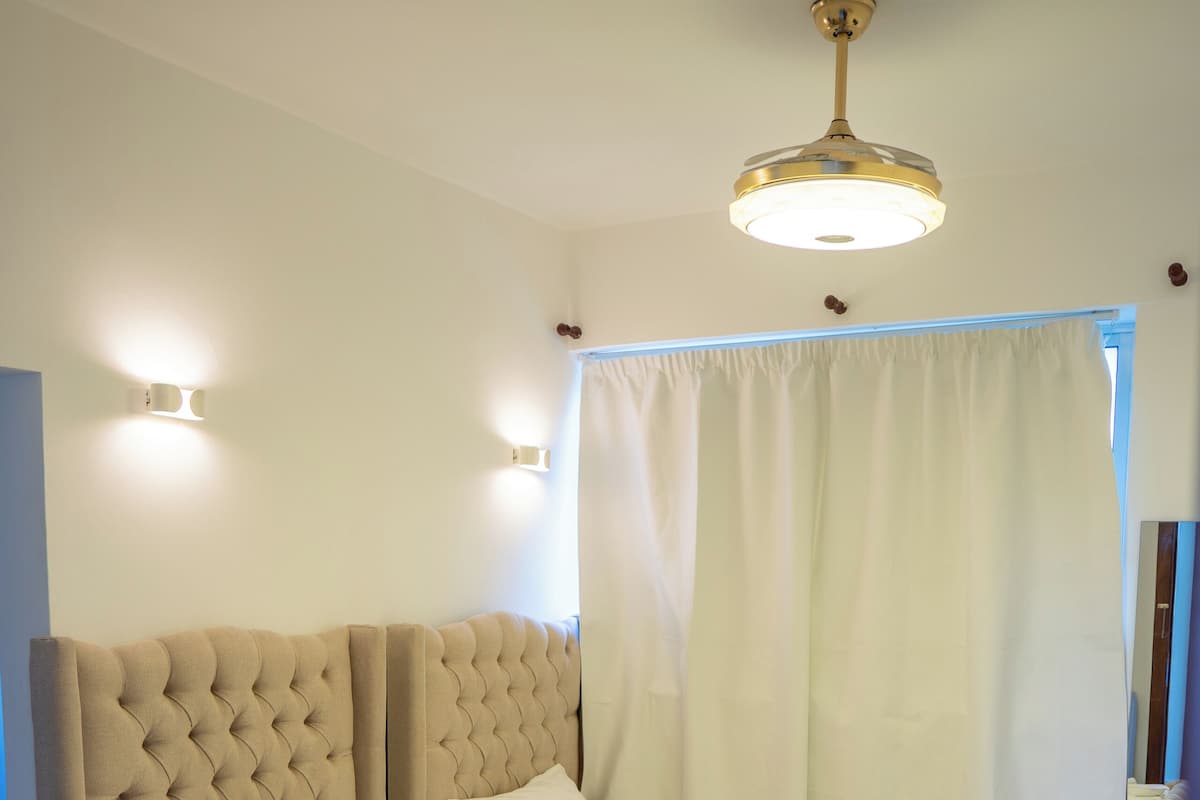 A hotel room with two beds, a ceiling fan, and a large window with curtains.