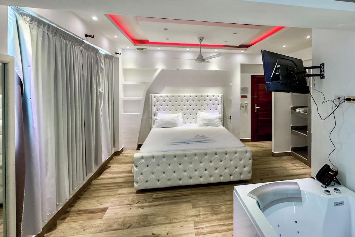 A modern bedroom with a large bed, a TV mounted on the wall, and a built-in bathtub.
