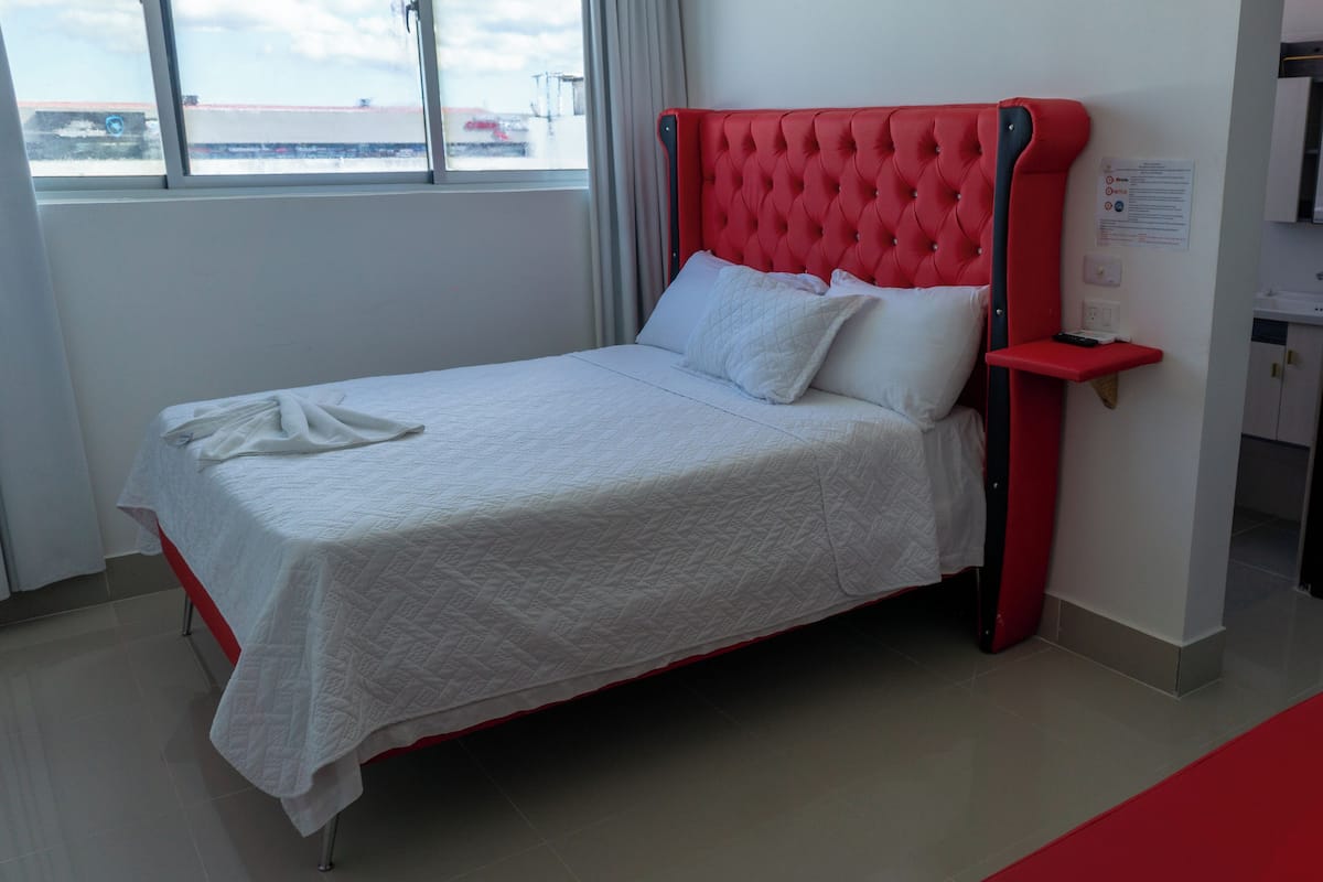A bed with a red headboard, white bedding, and a red nightstand.