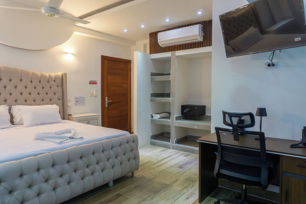 A hotel room with a large bed, a desk, a chair, a TV, and built-in shelves.