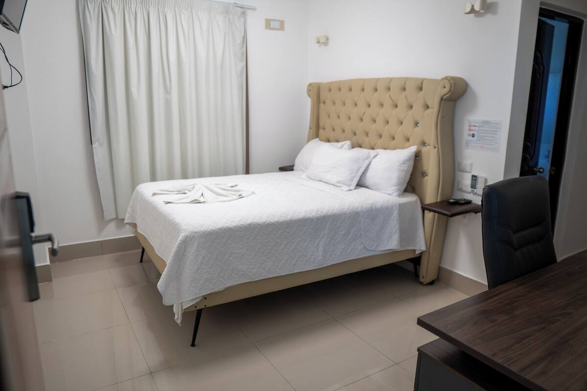 A neatly made bed with white linens, a tufted headboard, and a bedside table with a lamp.