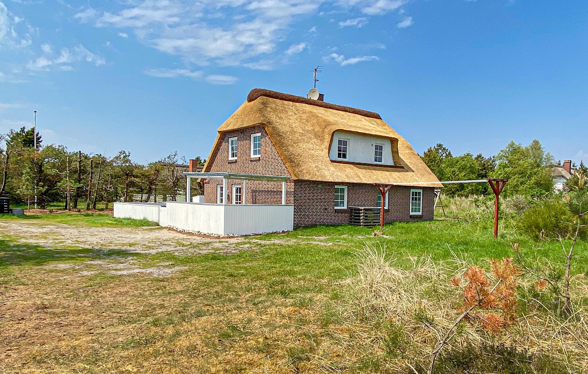 Een huis met rieten dak, een omheinde tuin en een schotelantenne.