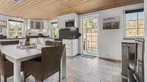 Eine moderne Küche mit weißen Schränken, ein Essbereich mit Korbstühlen und Blick ins Freie durch große Fenster.
