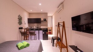 A compact hotel room with a bed, a TV, a small kitchenette, and a seating area. - Estudio Mar'Bella 2 min Praia Caminho de Moisés com Garagem e ArCond (Maragogi)