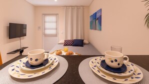 A hotel room with a bed, a TV, a breakfast setup with croissants and orange juice, and a painting on the wall. - Estudio Mar'Bella 2 min Praia Caminho de Moisés com Garagem e ArCond (Maragogi)